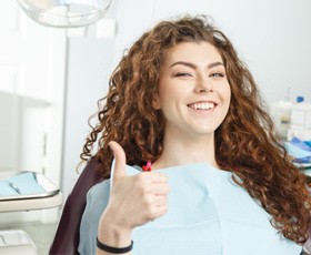 A young woman in a dentist’s chair smiling and giving a thumbs up